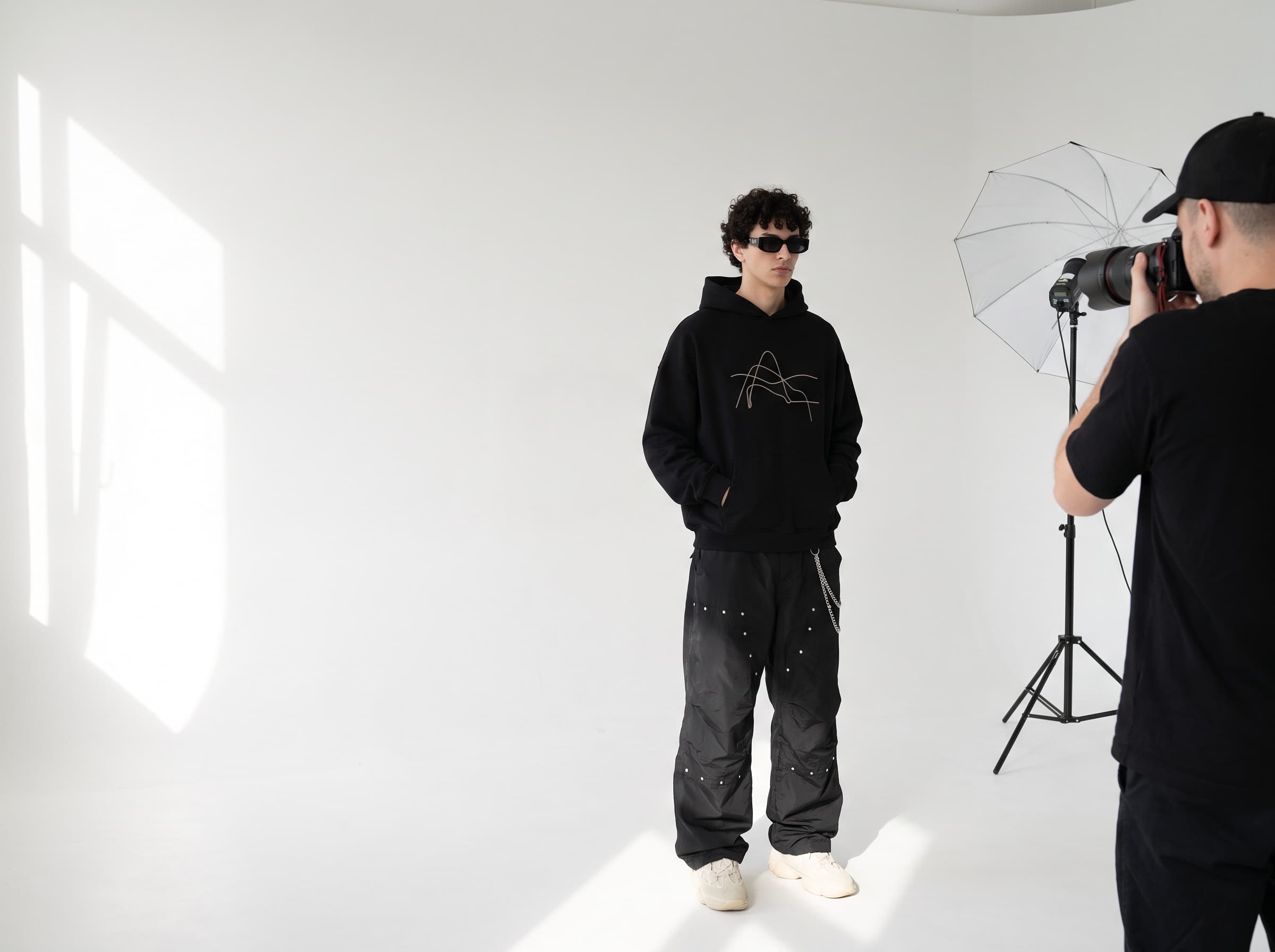 Veyra studio shoot — photographer directing a streetwear model on a white cyc wall